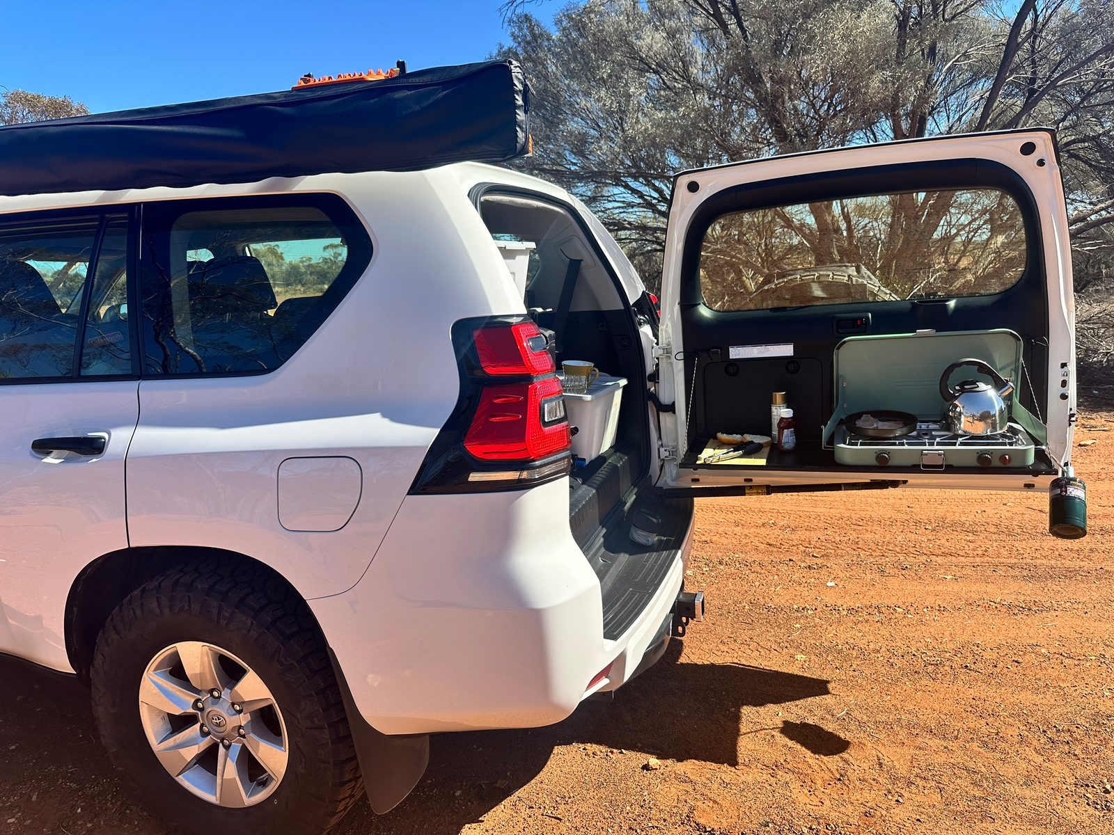 Kalgoorlie to Leonora: The Last Day of Never Having Swung a Detector Camp stove on a Toyota Prado tailgate cooking bacon beside a red dirt road