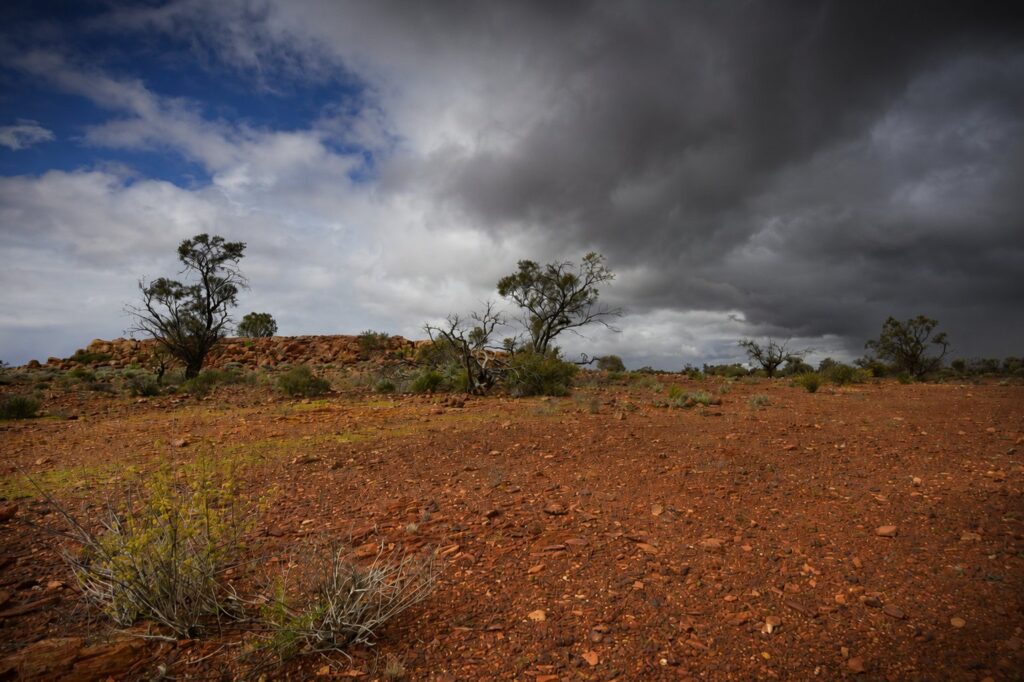 A dark storm band over low scrub and red gravel in the Western Australian goldfields.