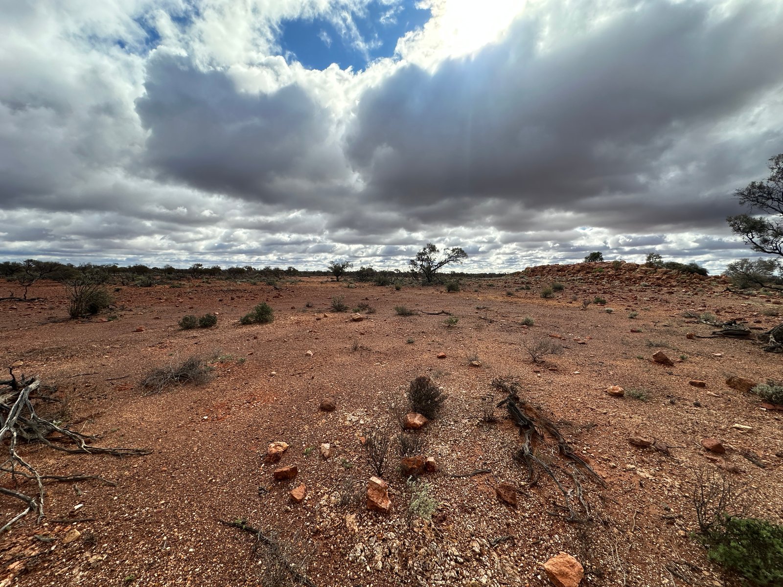 Sunlight breaking through heavy cloud over a stony red plain, with visible rays.