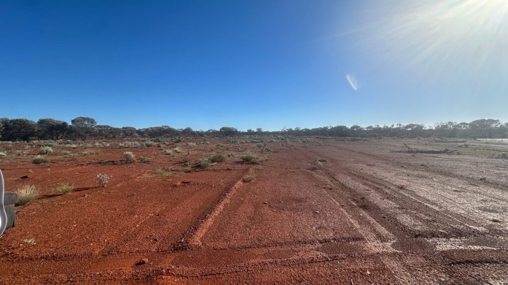 Red cleared ground with tyre tracks under a huge blue sky and a low morning sun in the WA goldfields.