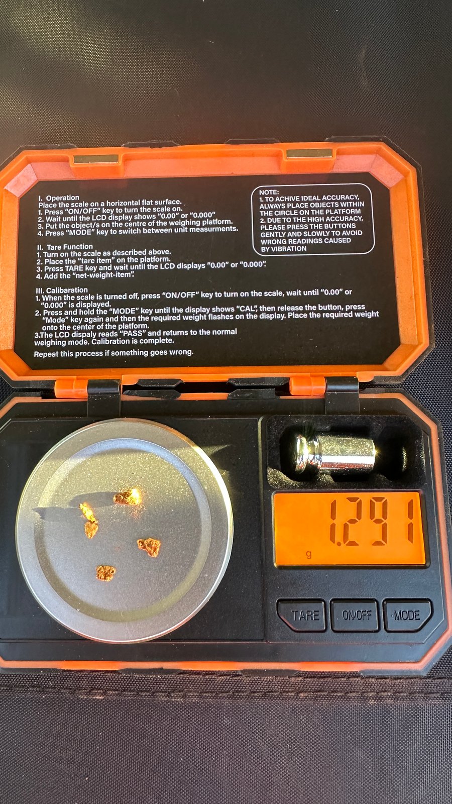 An open pocket scale with four small gold pieces on the pan, reading 1.291 grams, with the calibration weight beside it.
