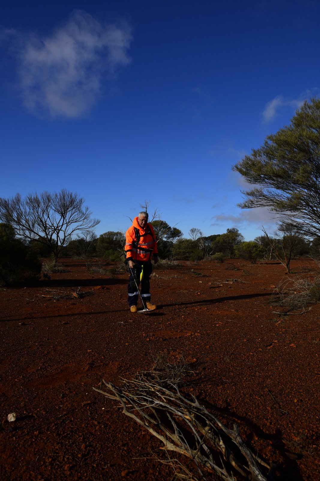 Rob in a hi-vis jacket standing on red dirt facing the camera, under a deep blue sky.